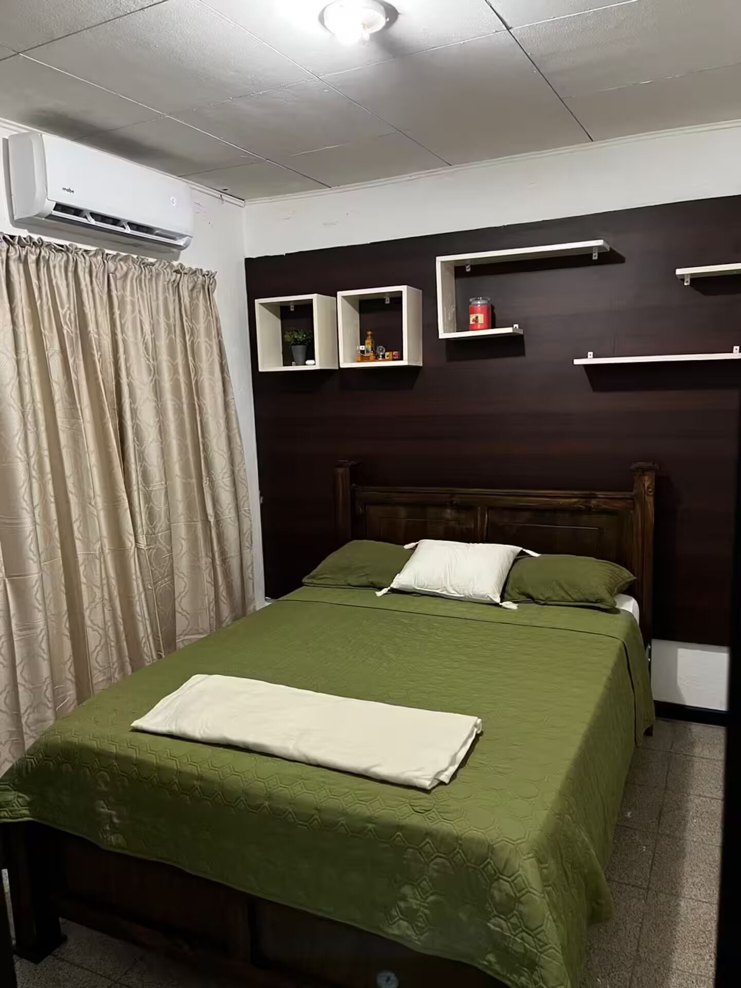 A bedroom with a bed, a headboard, a window with curtains, and wall-mounted shelves.