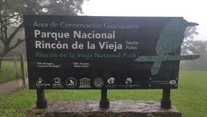 Schild für den Nationalpark Rincón de la Vieja, mit einer Vogel-Skulptur und Logos verschiedener Organisationen.