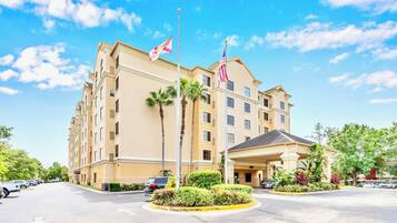 Um hotel de vários andares com fachada bege, palmeiras e duas bandeiras.
