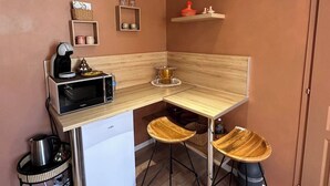 Eine kompakte Küchenzeile mit Mikrowelle, Wasserkocher und Kaffeemaschine, zwei Barhocker und einer kleinen Ablage mit Küchenutensilien.