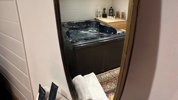 Ein Badezimmer mit einem großen Spiegel, der eine Badewanne reflektiert, einem Handtuchhalter mit Handtüchern und einer Wandleuchte.