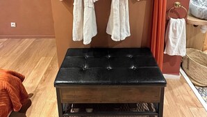 Ein Zimmer mit zwei weißen Bademänteln, die an einer Wand hängen, einer schwarzen gepolsterten Bank und einem Holzboden.