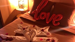 Ein Bett mit einem 'Love'-Schild, weißen Handtüchern, Rosen und einer roten Geschenkbox.