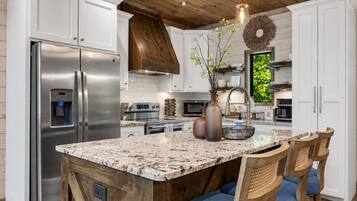 Una cocina con un refrigerador de acero inoxidable, un dispensador de agua integrado, una isla grande con asientos y un techo de madera.