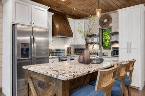 Una cocina con un refrigerador de acero inoxidable, un dispensador de agua integrado, una isla grande con asientos y un techo de madera.