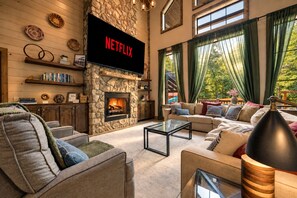 A cozy living room with a stone fireplace, a television displaying 'NETFLIX,' and a large window with curtains.