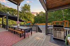 Una terraza techada al aire libre con una parrilla, una mesa de picnic y juegos infantiles.