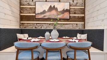 A dining area with a wooden wall, a painting, a vase with plants, and a table set for three.