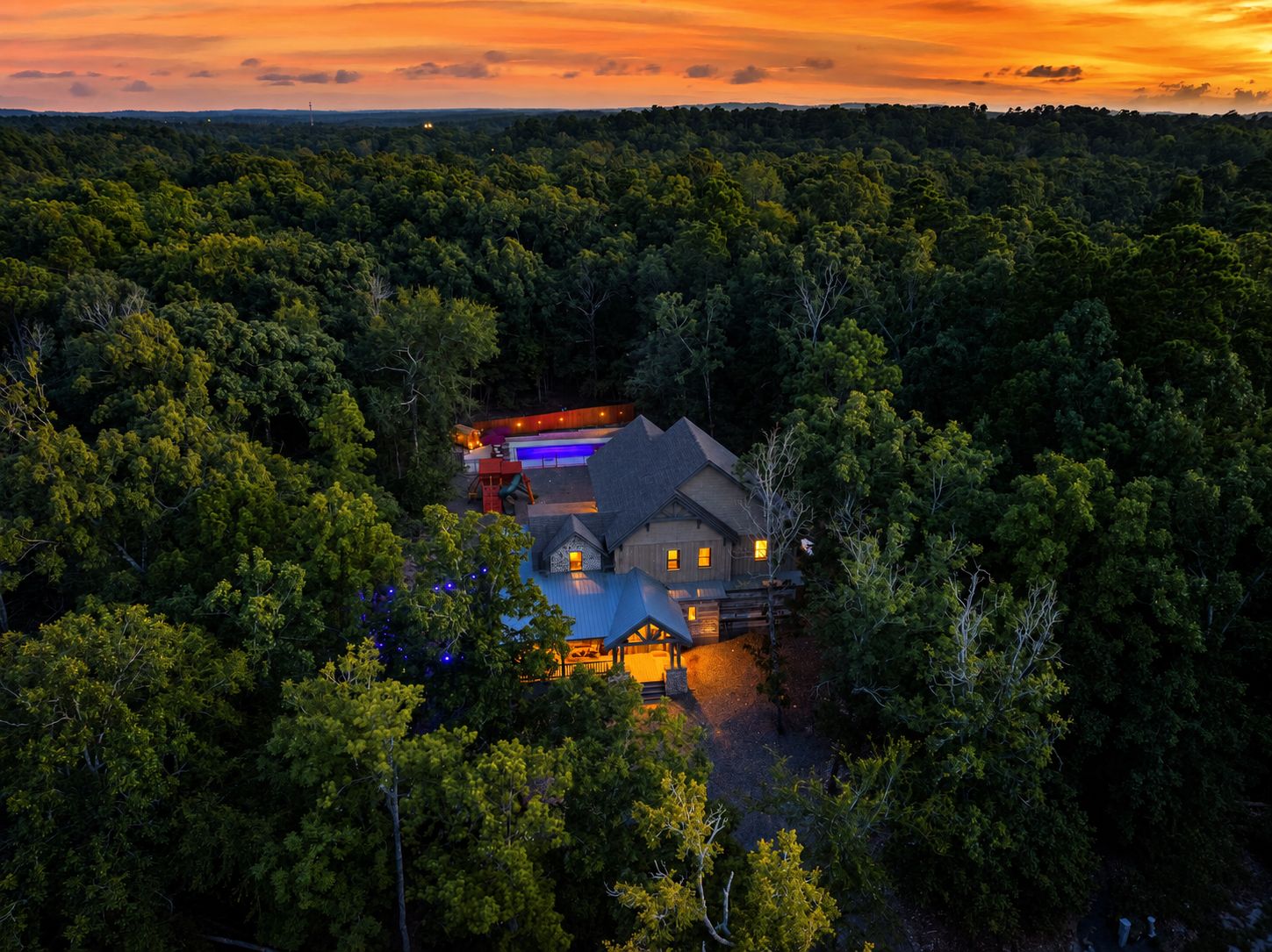A secluded cabin surrounded by dense forest, with a visible swimming pool and a deck area.