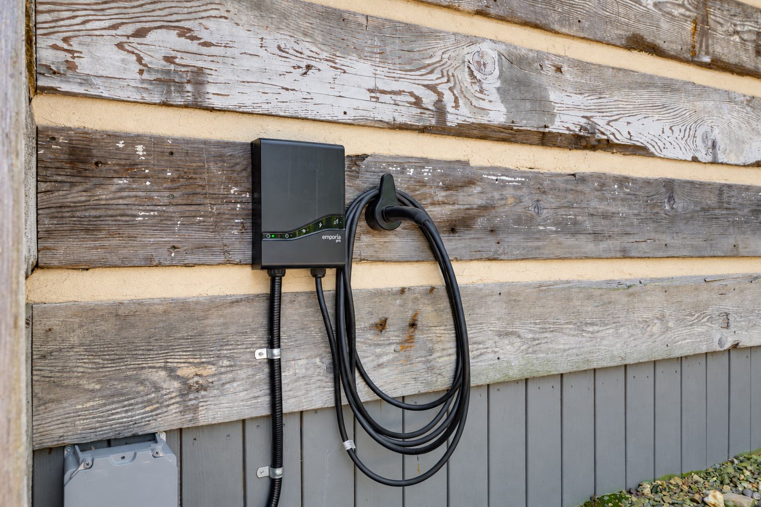 Un cuadro eléctrico exterior fijado a una pared de madera con un cable negro conectado.