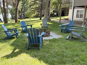 Un braciere circondato da poltrone Adirondack in una zona erbosa, con alberi e un edificio sullo sfondo.