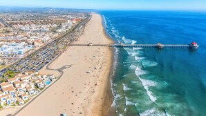 An aerial view of a coastal city with a long pier extending into the ocean, a sandy beach, and residential buildings along the shore. - Huntington Beach Surf Shack - Surf City, U.S.A. - Legal Rental (Huntington Beach)