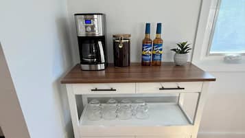A white wooden cart with a coffee maker, two bottles of Torani syrup, and a jar of honey.