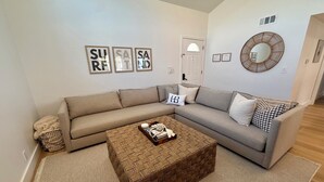 A living room with a beige sectional sofa, a woven coffee table, and framed artwork on the wall. - Huntington Beach Surf Shack - Surf City, U.S.A. - Legal Rental (Huntington Beach)