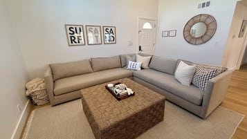 A living room with a beige sectional sofa, a woven coffee table, and framed artwork on the wall.