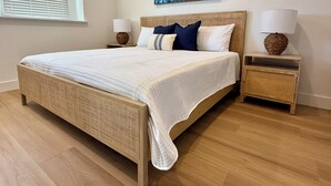 A bedroom with a large bed, two bedside tables with lamps, a window with blinds, and a wall-mounted artwork. - Huntington Beach Surf Shack - Surf City, U.S.A. - Legal Rental (Huntington Beach)