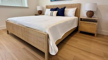 A bedroom with a large bed, two bedside tables with lamps, a window with blinds, and a wall-mounted artwork.