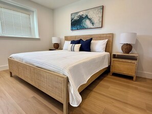 Um quarto com uma cama grande, duas mesas de cabeceira com luminárias, uma janela com persianas e uma obra de arte na parede.