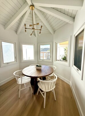 Uma sala de jantar com mesa de madeira, cadeiras brancas e um lustre.