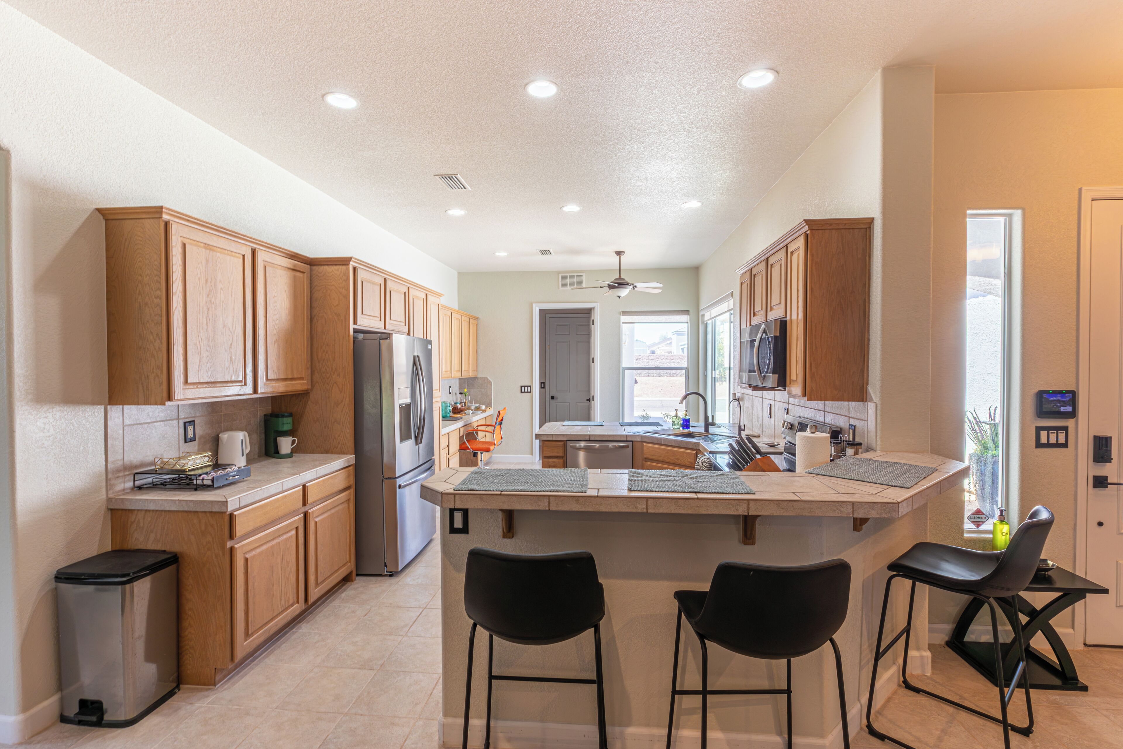 A modern kitchen with wooden cabinets, a stainless steel refrigerator, a dishwasher, and a central island with bar stools.