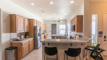 A modern kitchen with wooden cabinets, a stainless steel refrigerator, a dishwasher, and a central island with bar stools.