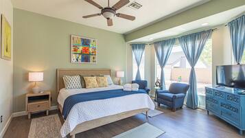 A bedroom with a bed, nightstands, a ceiling fan, a TV, a chair, a dresser, and a window with curtains.