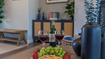 A wooden table with a fruit platter, two wine glasses, and a bottle of wine.