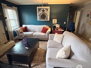 A living room with two white sofas, a dark coffee table, a patterned rug, and a wall-mounted artwork. - Cozy Ranch Retreat•1 Mile to DT Greer•Sleeps 8 (Greer)