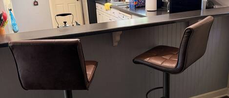 Eine Küche mit Barbereich, weißen Schränken, einem Kühlschrank und zwei Barhocker.