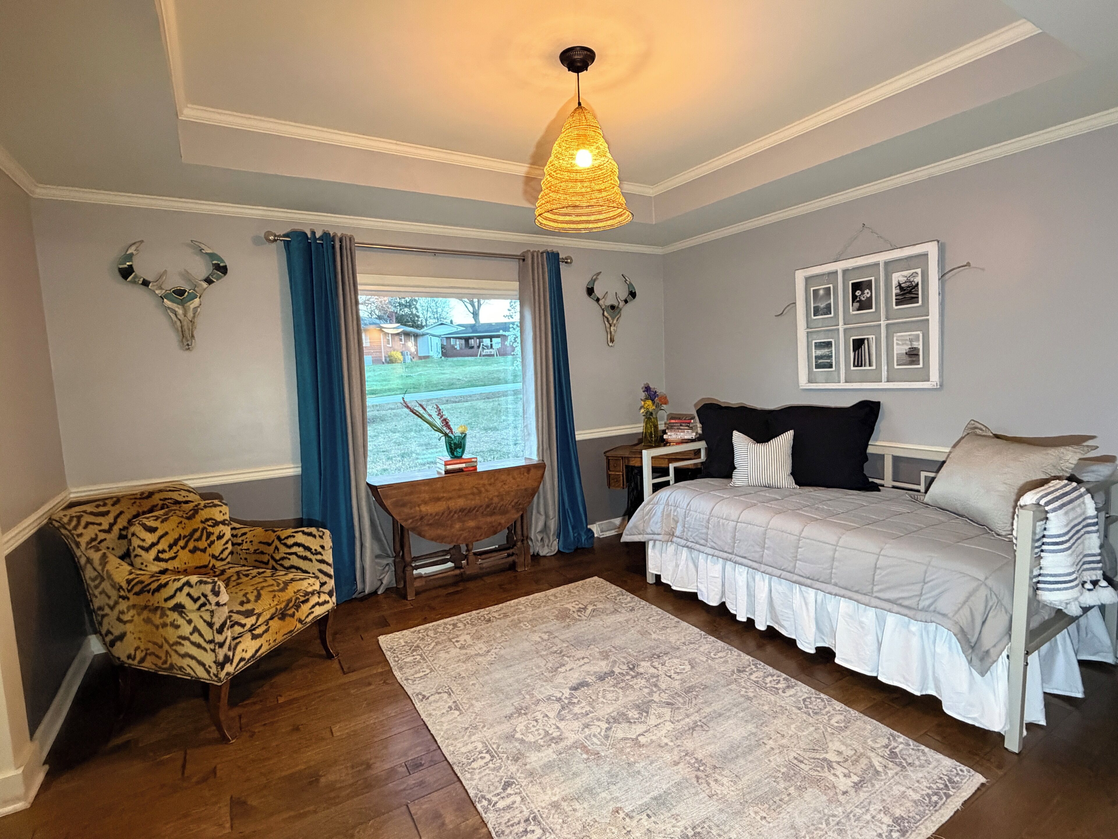 A bedroom with a bed, a chair, a rug, a window with curtains, and wall-mounted decor.