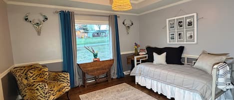 A bedroom with a bed, a chair, a rug, a window with curtains, and wall-mounted decor.