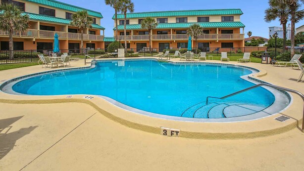 A swimming pool with a 3 FT depth marker, surrounded by lounge chairs and palm trees, with a building featuring balconies in the background. - Summer Deal: Free Tix and Beach Gear Credit (St. Augustine)