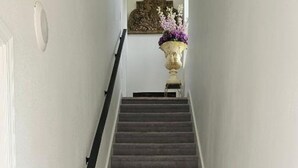 Een tapijt beklede trap met een leuning, die leidt naar een overloop met een decoratieve vaas en wanddecoratie.