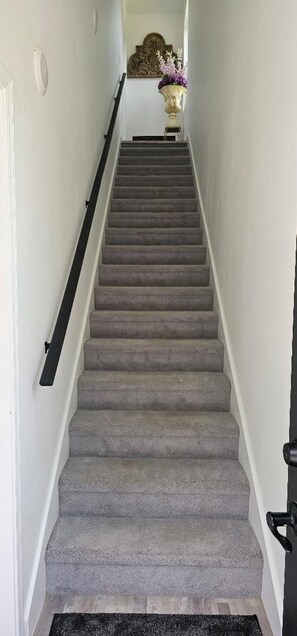 Eine Teppichstiege mit Handlauf, die zu einer Zwischenebene mit einer dekorativen Vase und Wandkunst führt.