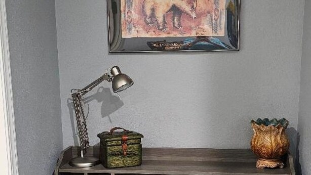 Een bureau met een stoel, een lamp, een ingelijst plaatje en een decoratief object op de plank.