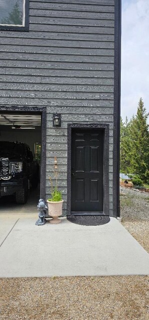 A house with a garage door open, a black front door, and a small garden with a statue and a potted plant. - Comfortable 1-bedroom apartment with AC in Hamilton with beautiful views (Hamilton)