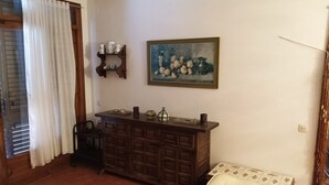 Een kamer met een houten kast, een stoel, een klein tafeltje, een schilderij en een plank met bekers.