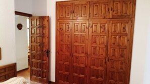 Een slaapkamer met een grote houten garderobe, een bed met beddengoed met een patroon, en een witte muur met een sterdecoratie.