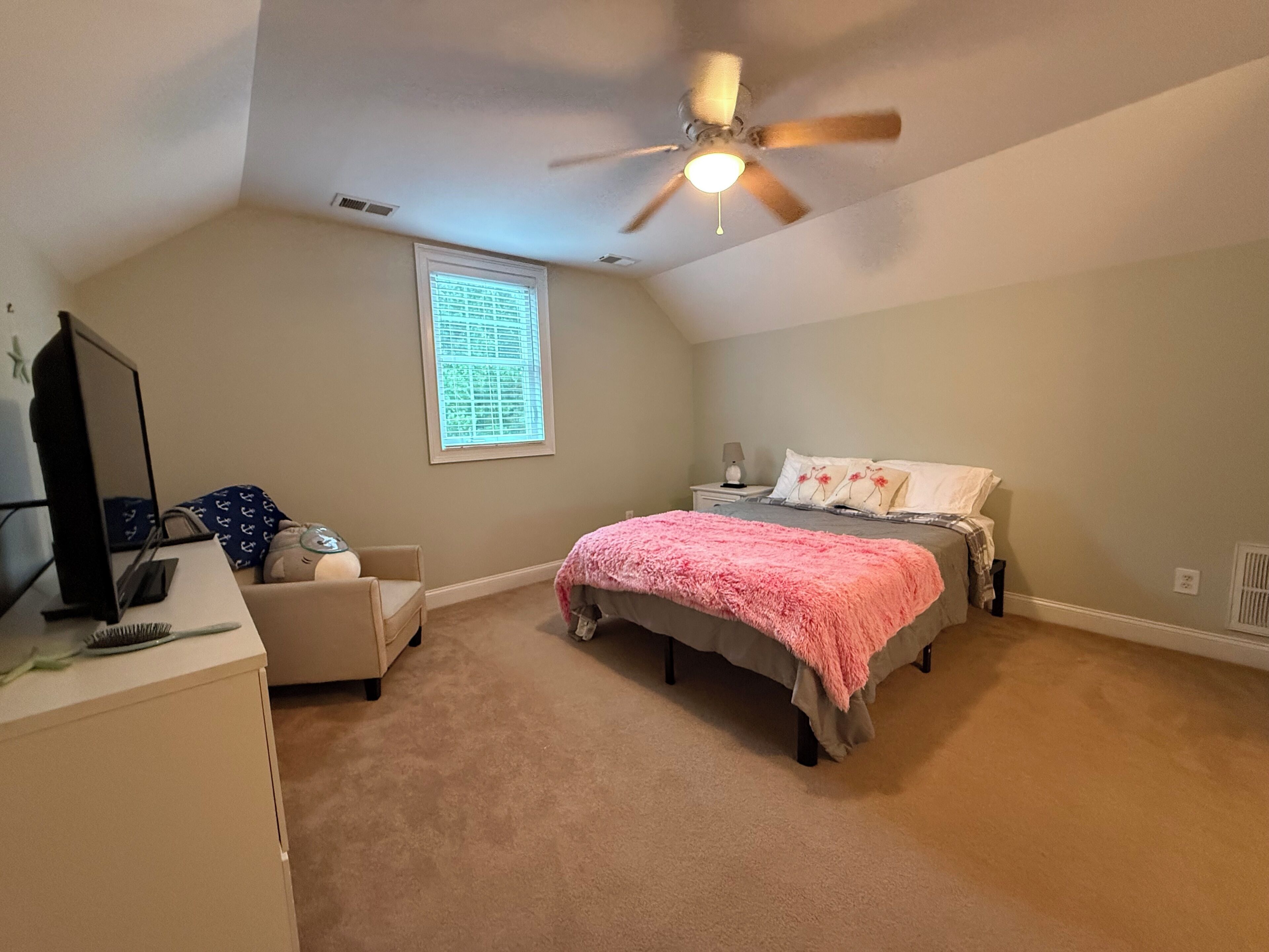 A bedroom with a bed, a desk, a chair, a ceiling fan, and a window.