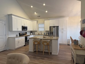 A modern kitchen with white cabinetry, stainless steel appliances, a central island with stools, and a wooden floor. - Pink Par-Tee Villa   Luxe Beach Getaway with Golf Cart (Murrells Inlet)