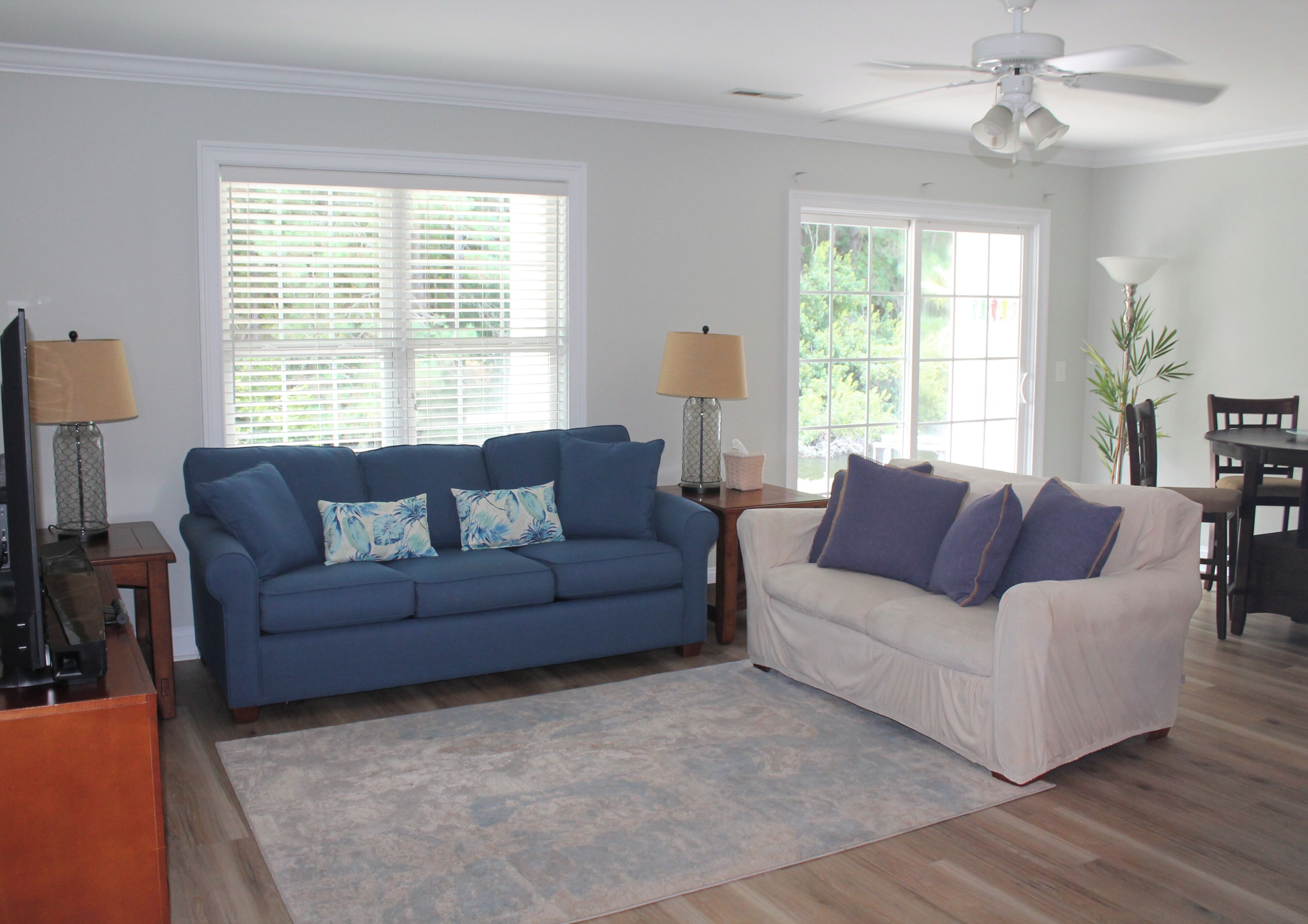 A living room with a blue sofa, a white sofa, and a ceiling fan.