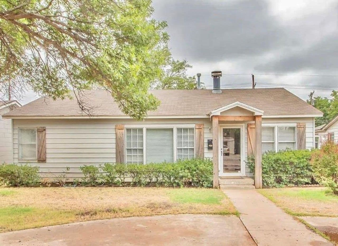 A single-story house with a front porch, a chimney, and a small front yard.