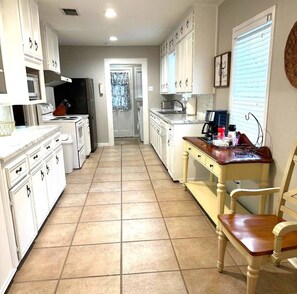 A kitchen with white cabinets, a stove, a microwave, and a dining area with a table and chairs. - Mackey Park Retreat! (Lubbock)