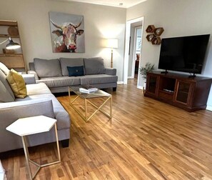 A living room with a sofa, coffee table, TV stand, and artwork. - Mackey Park Retreat! (Lubbock)
