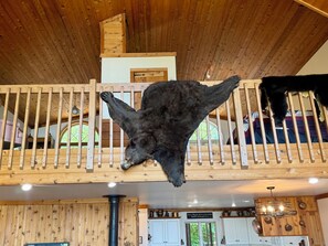 A wooden balcony with a mounted animal head, a chandelier, and a kitchen area with cabinets and a sign. - Beautiful home, giant windows, sand beach, dock. Premier crystal clear lake. (Bemidji)