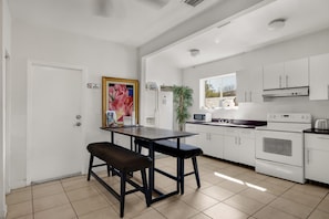 Una cocina moderna con armarios blancos, una mesa de comedor con bancos, un microondas, estufa y un ventanal grande.