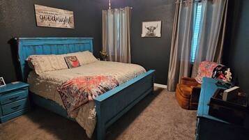 A bedroom with a bed, nightstands, a dresser, a ceiling fan, curtains, and a wall sign.