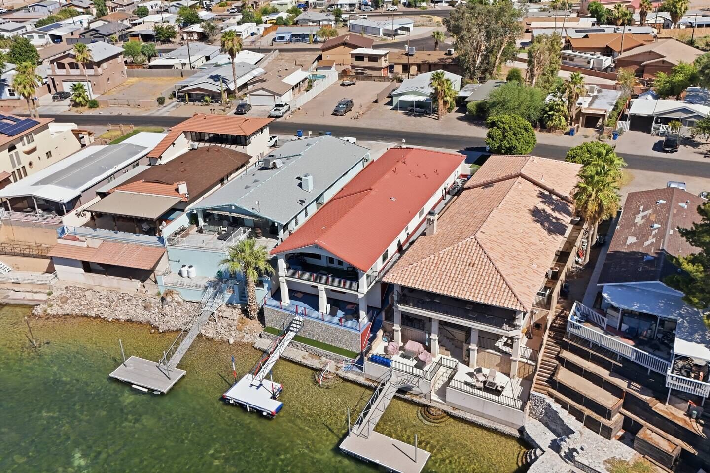 Un barrio residencial con una casa grande de techo rojo, un muelle y una piscina.