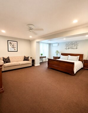A bedroom with a bed, a sofa, a small table, and a wall-mounted artwork.
