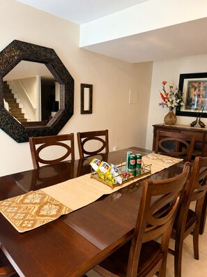 A dining area with a wooden table, chairs, a decorative mirror, and a vase with flowers.